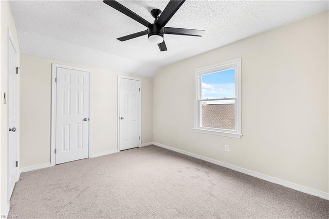 unfurnished bedroom featuring baseboards, vaulted ceiling, a textured ceiling, carpet floors, and multiple closets