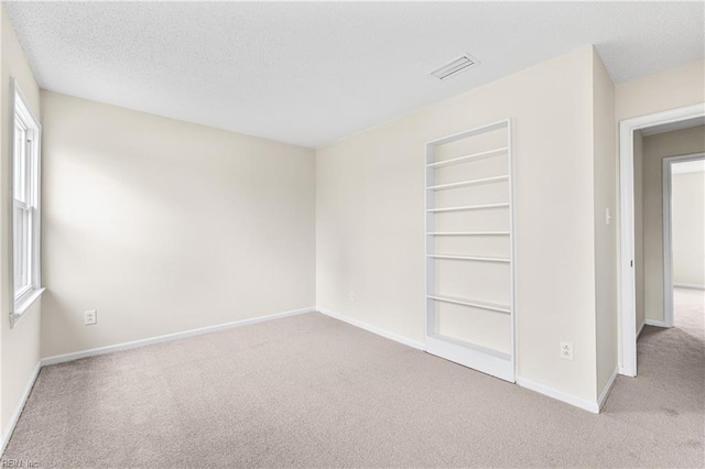 empty room with a textured ceiling, carpet, visible vents, and baseboards