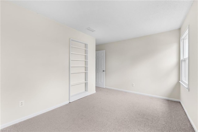 spare room featuring carpet floors, visible vents, and baseboards