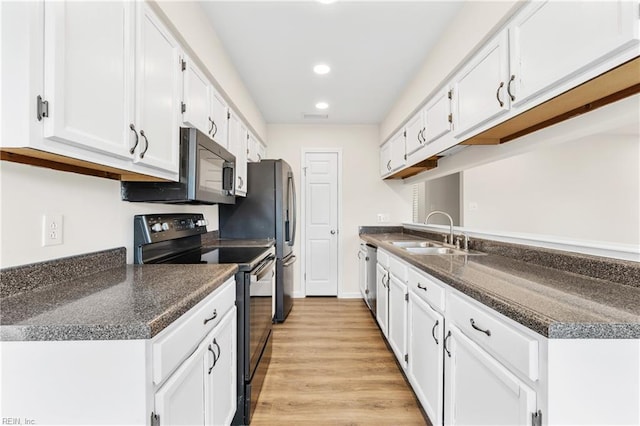 kitchen featuring stainless steel appliances, dark countertops, a sink, and white cabinetry