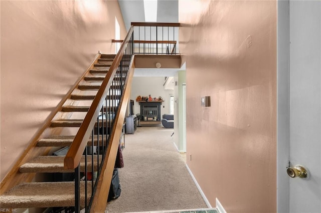 staircase featuring carpet, a glass covered fireplace, a high ceiling, and baseboards