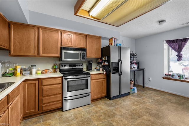 kitchen with brown cabinets, stainless steel appliances, light countertops, a textured ceiling, and baseboards