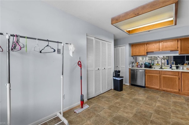 kitchen with light countertops, stainless steel dishwasher, a sink, and brown cabinets