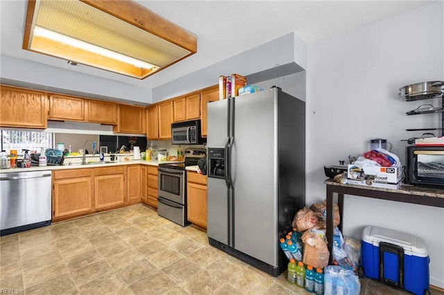 kitchen featuring brown cabinets, stainless steel appliances, a sink, and light countertops