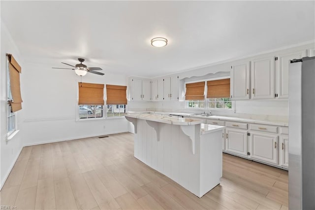 kitchen featuring a breakfast bar, a sink, a kitchen island, white cabinetry, and light wood finished floors