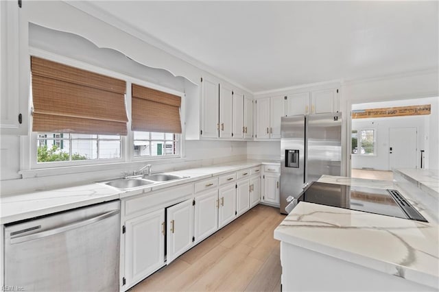 kitchen with light wood finished floors, appliances with stainless steel finishes, white cabinetry, a sink, and light stone countertops