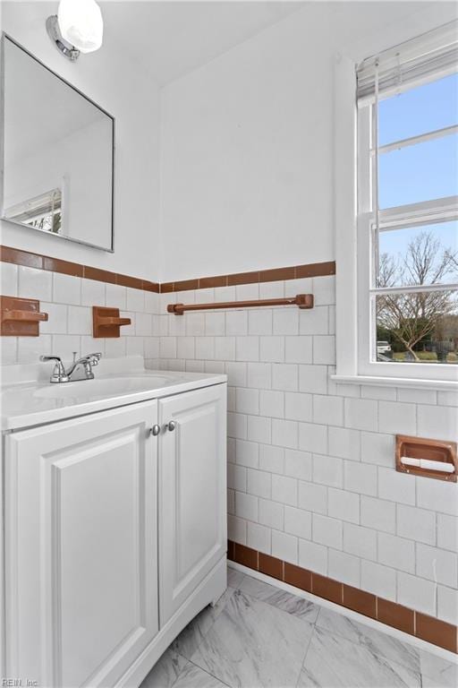 bathroom with marble finish floor, wainscoting, vanity, and tile walls