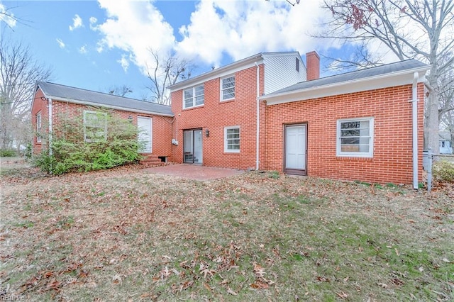 rear view of house with a yard, brick siding, a patio, and a chimney