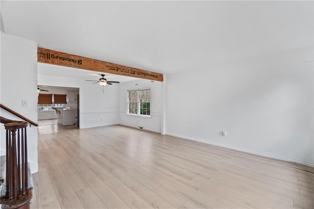 unfurnished living room with baseboards, a ceiling fan, light wood-style flooring, stairway, and beam ceiling