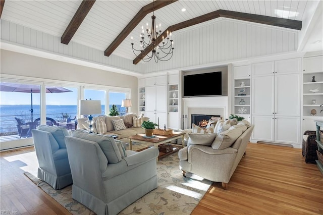 living area with built in features, beam ceiling, a notable chandelier, light wood-style floors, and a warm lit fireplace