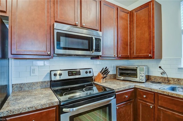 kitchen featuring a toaster, light countertops, decorative backsplash, appliances with stainless steel finishes, and a sink