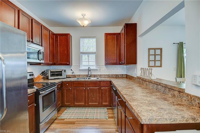 kitchen with a peninsula, a sink, appliances with stainless steel finishes, light wood-type flooring, and decorative backsplash