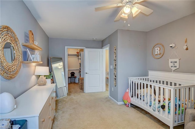 bedroom with light carpet, a crib, baseboards, a ceiling fan, and a spacious closet