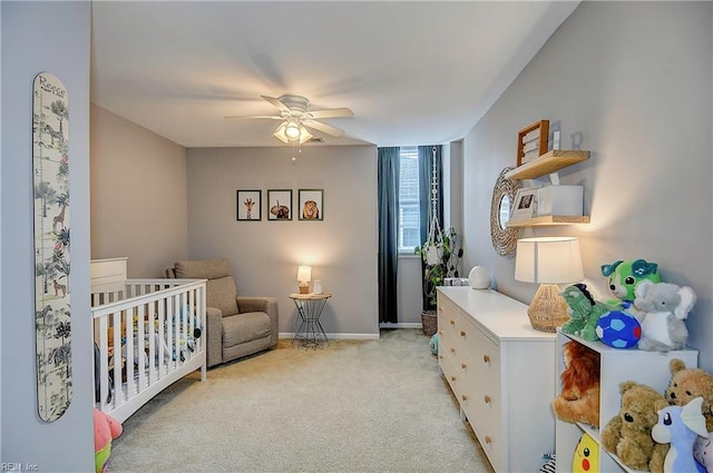 bedroom featuring light carpet, baseboards, a crib, and a ceiling fan