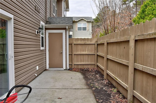 property entrance with a patio area, a shingled roof, and fence