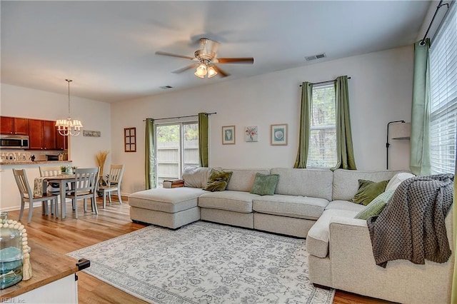 living room with ceiling fan with notable chandelier, a wealth of natural light, visible vents, and light wood-style floors