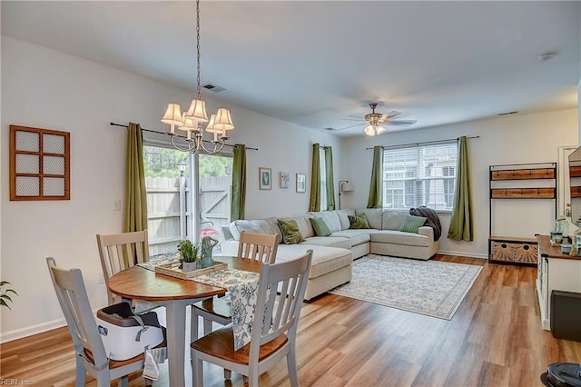 dining space with light wood-style floors, a wealth of natural light, visible vents, and ceiling fan with notable chandelier