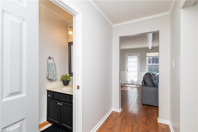 hall featuring a sink, dark wood-style floors, baseboards, and crown molding