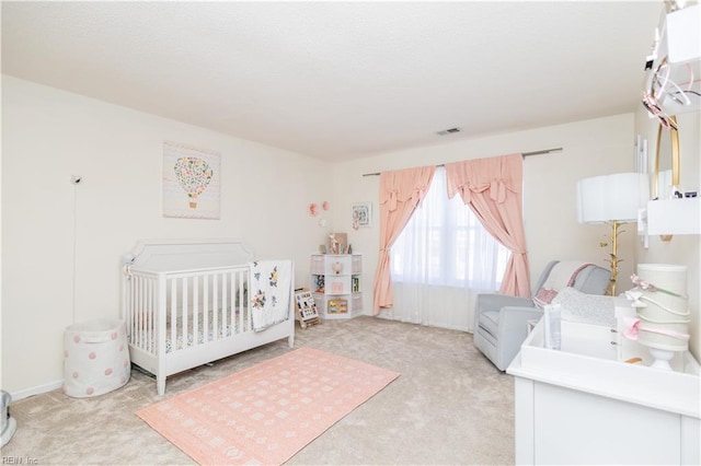 bedroom with a nursery area, visible vents, and light colored carpet