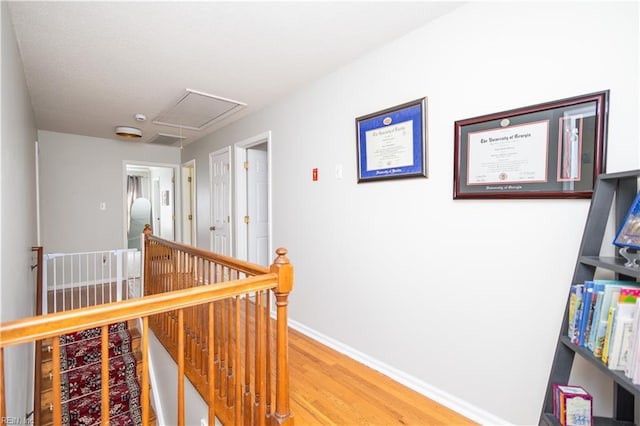 hall with light wood-type flooring, attic access, baseboards, and an upstairs landing