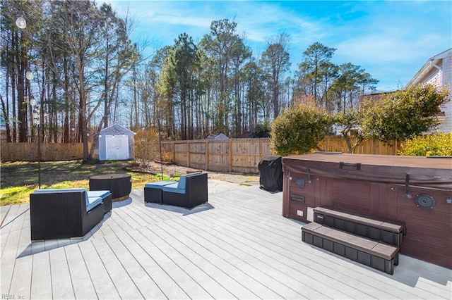 deck featuring an outbuilding, a storage unit, a fenced backyard, and a hot tub