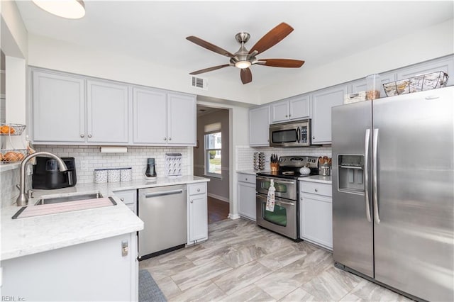 kitchen with stainless steel appliances, visible vents, decorative backsplash, a sink, and ceiling fan