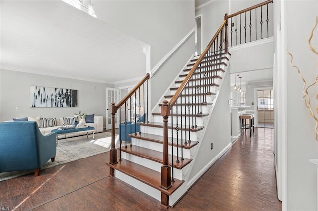 stairway featuring crown molding, a towering ceiling, baseboards, and wood finished floors