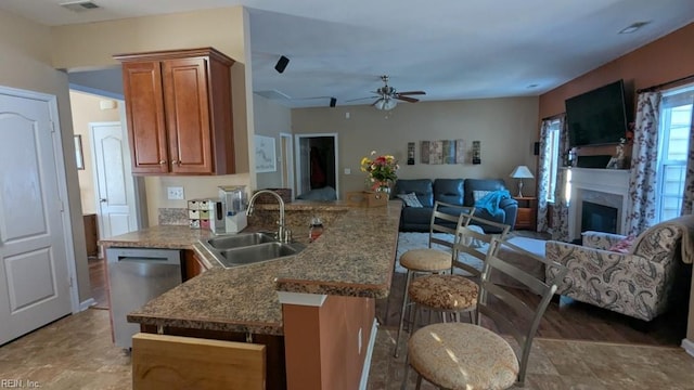 kitchen with brown cabinets, stainless steel dishwasher, a glass covered fireplace, open floor plan, and a sink