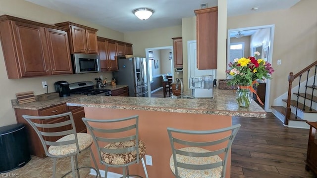 kitchen with a breakfast bar area, appliances with stainless steel finishes, wood finished floors, a peninsula, and a sink