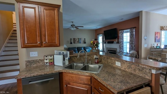 kitchen with a peninsula, a sink, open floor plan, dishwasher, and brown cabinetry