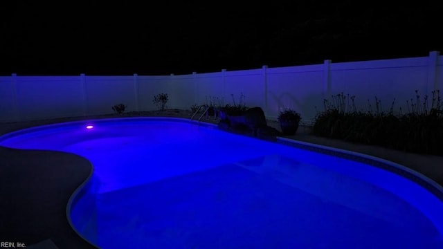 pool at night featuring a fenced backyard