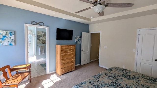 bedroom featuring baseboards, light colored carpet, ensuite bath, ceiling fan, and a tray ceiling