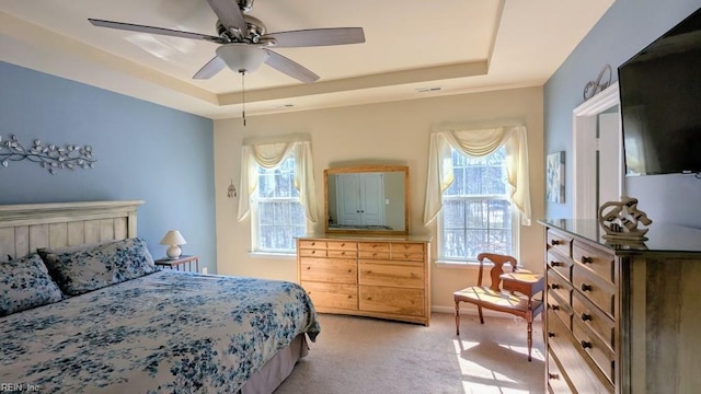 bedroom with a raised ceiling, light colored carpet, visible vents, ceiling fan, and baseboards