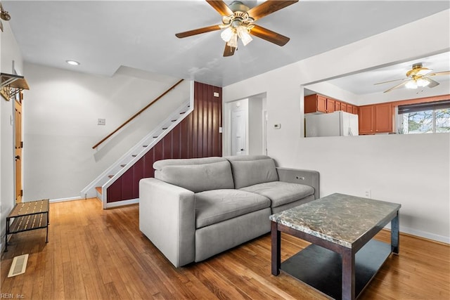 living room with stairway, wood-type flooring, visible vents, and a ceiling fan