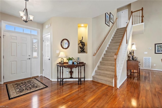 entryway with visible vents, baseboards, stairway, hardwood / wood-style floors, and a notable chandelier