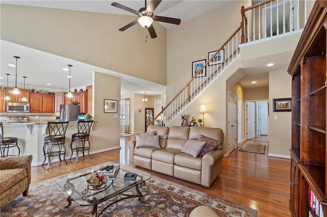 living room with ceiling fan, stairway, light wood-style flooring, and baseboards