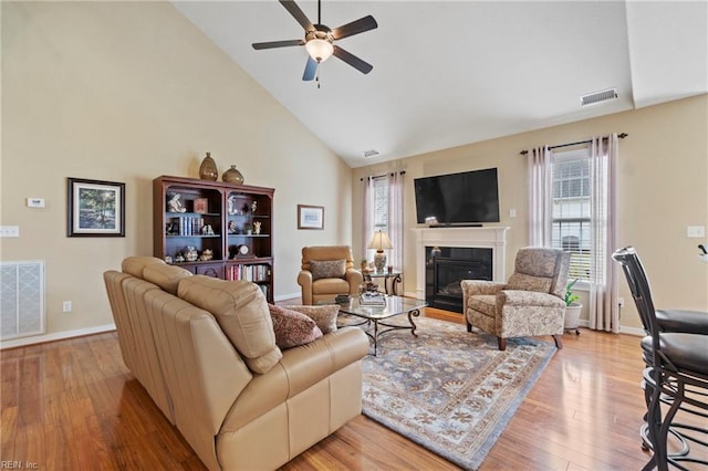 living room with high vaulted ceiling, visible vents, wood finished floors, and a glass covered fireplace