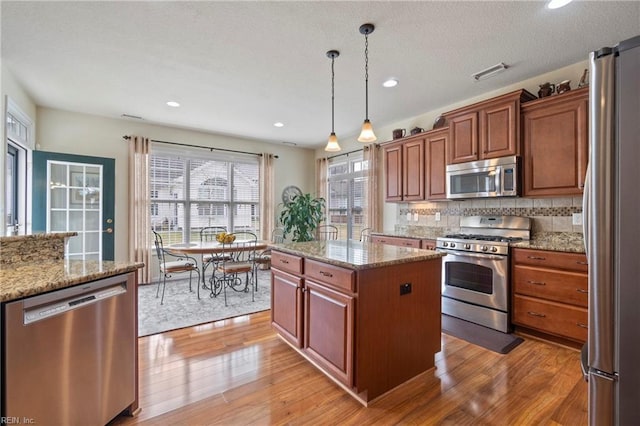 kitchen featuring stainless steel appliances, visible vents, hanging light fixtures, backsplash, and light wood finished floors