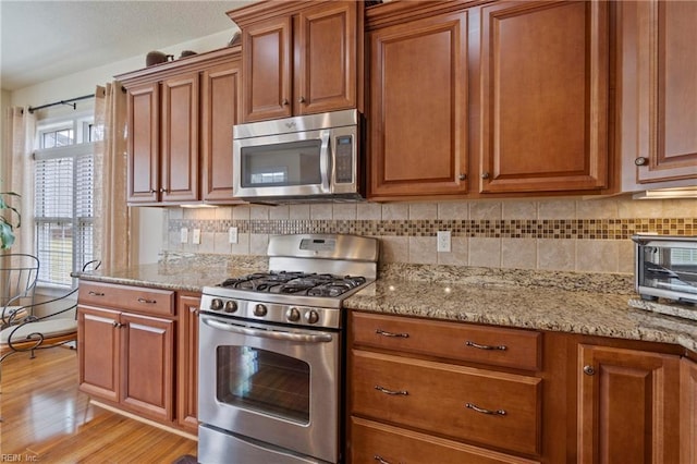 kitchen with stainless steel appliances, backsplash, brown cabinets, and light wood-style flooring