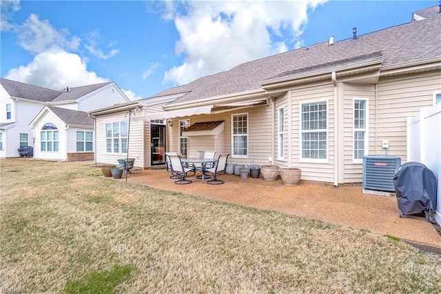 rear view of property featuring a yard, a shingled roof, central AC, and a patio area