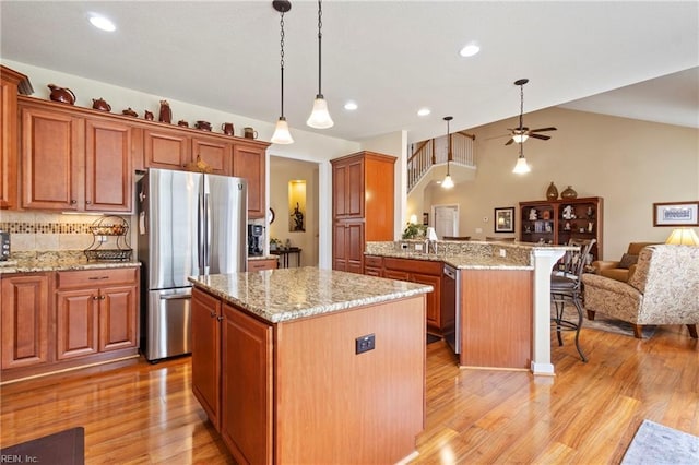 kitchen featuring open floor plan, a peninsula, appliances with stainless steel finishes, and light wood-style flooring