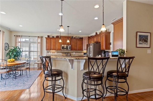 kitchen featuring decorative backsplash, light wood-style flooring, appliances with stainless steel finishes, a kitchen breakfast bar, and a peninsula