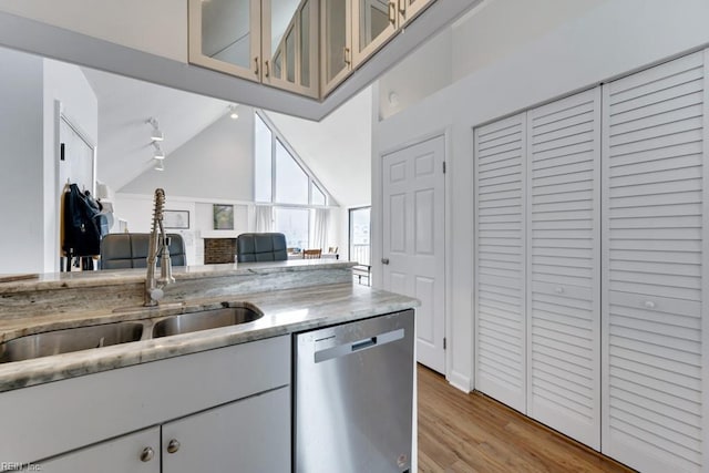 kitchen featuring light wood finished floors, light stone counters, stainless steel dishwasher, high vaulted ceiling, and a sink