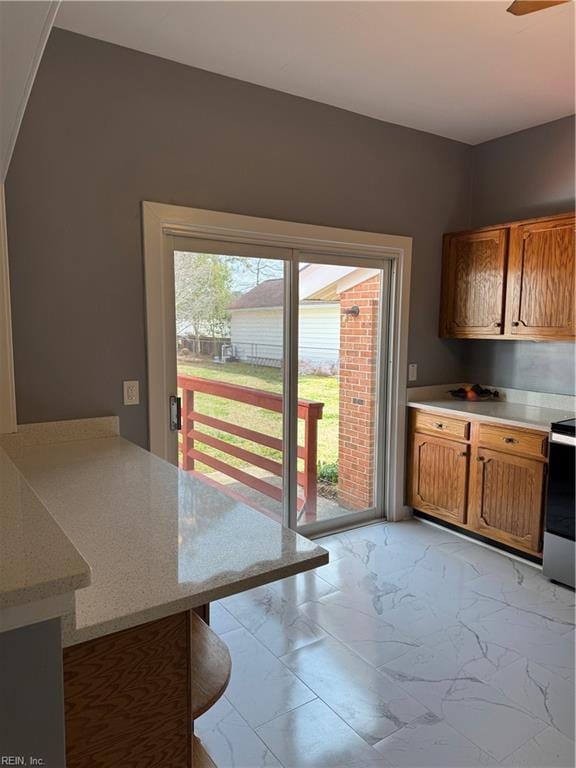 kitchen with a breakfast bar area, a peninsula, electric range, marble finish floor, and brown cabinetry