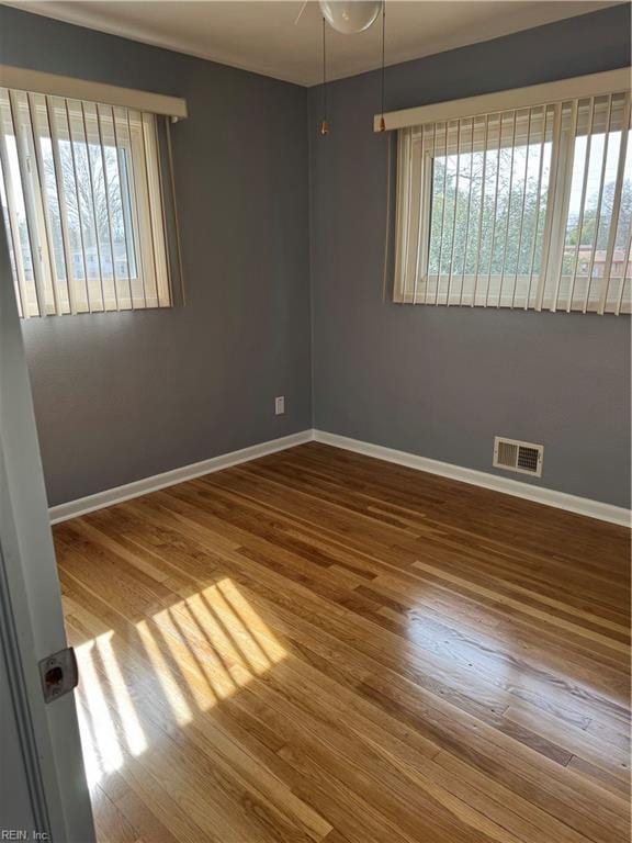 unfurnished room featuring baseboards, wood finished floors, visible vents, and a healthy amount of sunlight