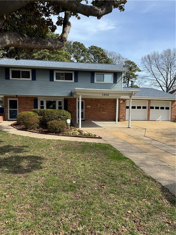 traditional home featuring a garage, driveway, brick siding, and a front yard