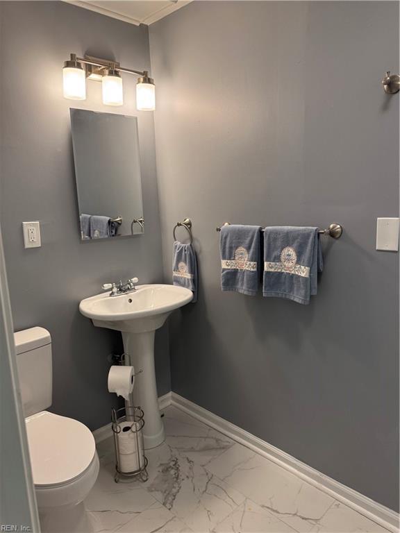 half bath with marble finish floor, a sink, toilet, and baseboards