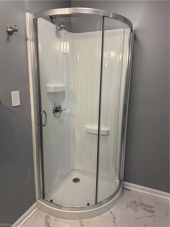 bathroom featuring marble finish floor, a shower stall, and baseboards