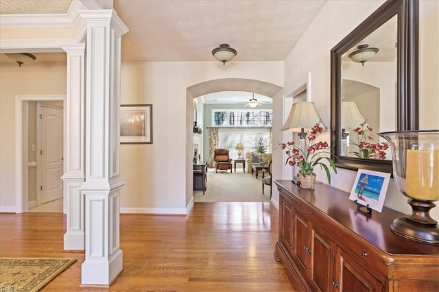 hallway featuring arched walkways, light wood-style flooring, baseboards, and ornate columns