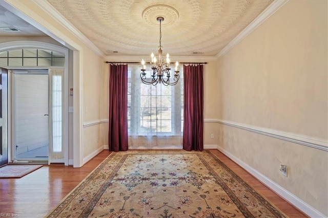 unfurnished dining area with visible vents, ornamental molding, an inviting chandelier, and wood finished floors